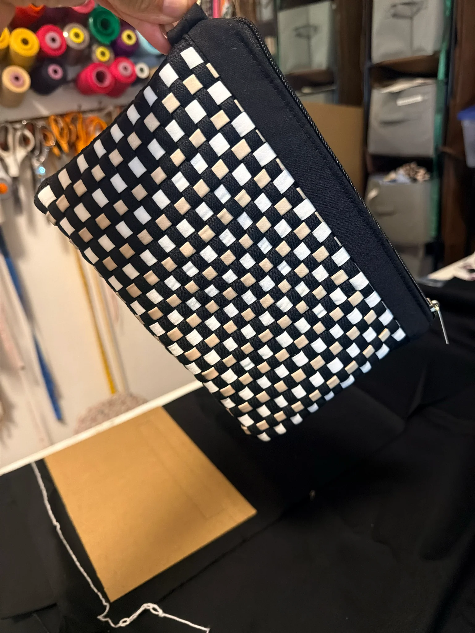Black clutch with a woven pattern in black, white and tan, and a black edge with a silver zipper